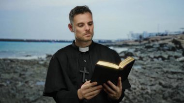 Papaz kayalık sahilinde açık bir kitapla kitap okuyor, sakin sahil atmosferini yakalıyor..