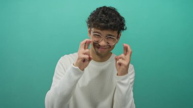 Latin kökenli genç adam beyaz süveter ve gözlük giyerek stüdyoda şans diliyor..