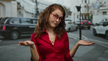 Kırmızı saçlı ve gözlüklü bir kadın Londra 'nın işlek bir caddesinde duruyor. Trafiğin ortasında düşünceli bir ifadeyle elini uzatıyor..