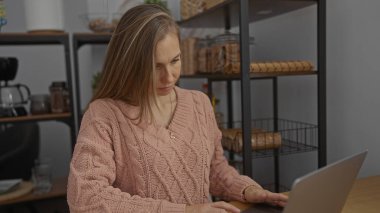 Genç bir kadın kapalı bir ofiste bilgisayar işine odaklanmış. Raflar ve modern dekorlar, üretken ve profesyonel bir atmosferi yansıtıyor..