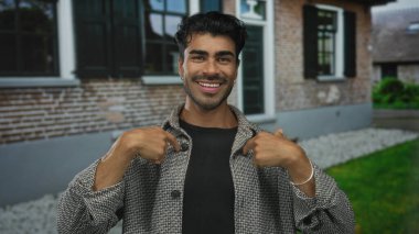 Tuğla evin girişinde, gün ışığında, kararlı bakışlarla, kendine güvenle göğsünü gösteren bir adam..