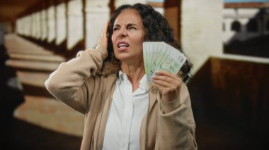 Üniversitede orta yaşlı bir kadın elinde Singapur banknotları tutarken akademik ortamda maddi stresin göstergesi olarak acı dolu bir ifade kullanıyordu..