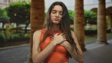 Gün batımında kemer ve kolları olan bir avluda, turuncu kolsuz üst göğsü olan genç İspanyol kadın. Acı..