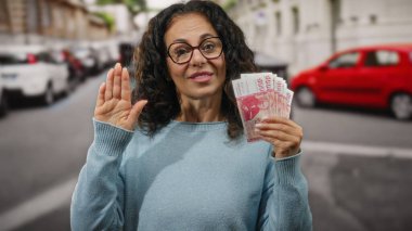Bir şehir caddesinde elinde İzlanda Krona banknotları tutan kadın yemin jesti olarak elini kaldırıyor. Açık havada güven ve finansal bağlılığı simgeliyor..