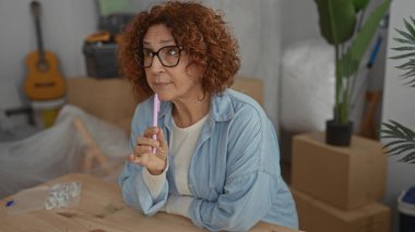 Çağdaş oturma odasında kutuların, gitarların ve bitkilerin arasında yeni bir dairede kafa yoran bir kadın..