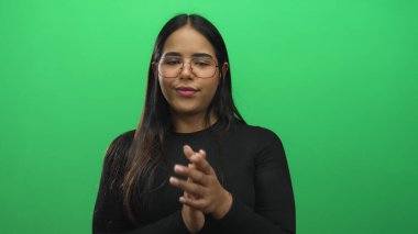 Yeşil bir sette el çırpan kadın elleri, pürüzsüz bir arka plan duvarına karşı izole edilmiş genç bir Latin Latin modelini gösteriyor..