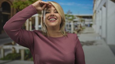 Önüne bakarken, parlak güneş ışığı altında, meşgul şehir caddesinde elleri ile gözleri koruyan kadın, beklenti merakı.