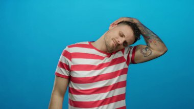 Parlak mavi duvara karşı çizgili gömlekli genç adam rahat ve düşünceli görünüyor. Kafası eğik, rahat ve dışa dönük bir tavır sergiliyor.