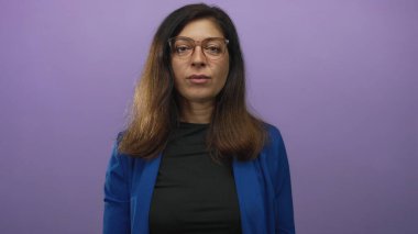 Ciddi bir ifade takınan, mavi ceketli İspanyol kadın mor stüdyoda selam vermek için el ele tutuşuyor..