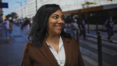 Şehir merkezindeki kalabalık bir sokakta gün ışığında dişlerini gösteren kahverengi ceketli bir kadın gülümsüyor; sevinç iyimserliği.