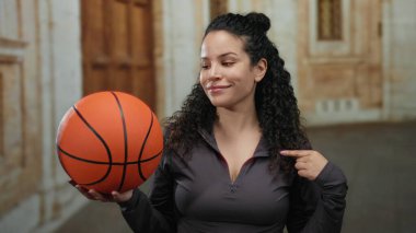 Eski bir üniversite avlusunda İspanyol bir kadın elinde basketbol topuyla kendini göstererek atletik ruhu ve akademik arkaplanı canlandırıyor..