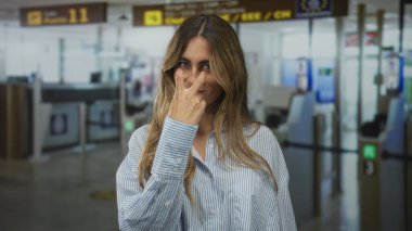 Sarışın, dalgalı saçlı, başı eğik, mağazada çizgili gömlek giyen, kendine güvenen bir kadın..