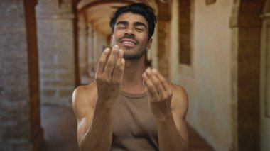 Elleri çimdiklenmiş parmaklarla gezen adam, taştan duvarları olan, güneşli, dar, eski kasaba koridorlarında el hareketi yapıyor..