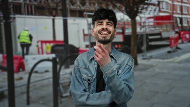 Genç bir adam açık hava inşaatında duruyor, kot ceket giyiyor, yakışıklı ve rahat poz veriyor..