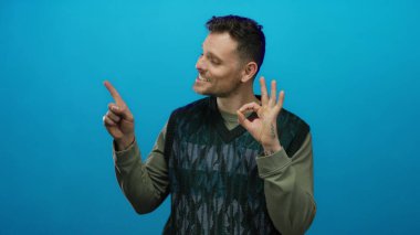 Hispanik bir adam gülümsüyor ve iyi bir jest yapıyor canlı mavi bir arka plana karşı yan işaret ederken, pozitiflik ve güven iletiyor.