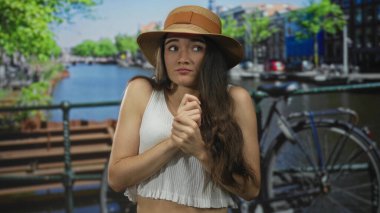 Hasır şapkalı bir kadın yazın, bisiklet sürerken, hareketli bir caddede, kanal korkuluklarıyla ellerini çırpıyor; gerginlik..