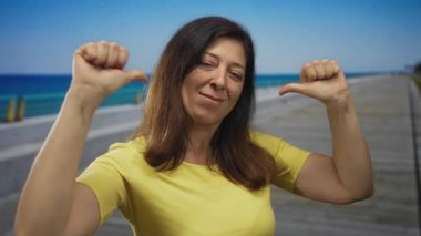 Sarı tişörtlü kadın, deniz kenarında deniz kenarında deniz kenarında yürümeyi işaret ediyor..