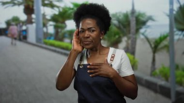 Önlük giymiş bir kadın sahilde palmiye ağaçlarıyla dikiliyor. Sahilde yürürken ve konuşurken, sakin bir okyanus manzarasıyla duyguları iletiyor..