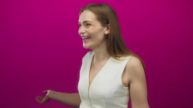 Kadın gülümsüyor ve parlak pembe duvarları olan parlak bir stüdyoda el dürbünü hareketi yapıyor; merak.