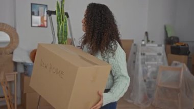 Yeni evin içinde bir kutu taşıyan bir kadın. Parlak oturma odasındaki eşyalarla dolu. Dairesinde yeni bir başlangıç yapıyor..