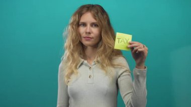 Kadın elini bir stüdyo alanını işaret etmek için kullanıyor. Sarı genç pozunu sunuyor. Üzerinde sarı bir vergi hatırlatması var..
