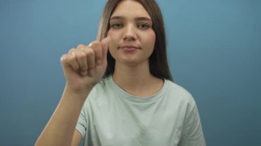 Mavi stüdyoda elini kaldırmış ve parmaklarını hafifçe öne doğru gösteren bir kız, sessiz tefekkür.