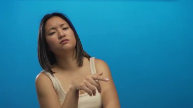 Katı mavi bir duvara bakan, el hareketleriyle ifade eden bir kadın, parlak bir stüdyo ortamının altında derin bir düşünce ve merak anı yakalıyor, izole edilmiş bir düşünce senaryosunu aktarıyor..