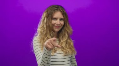 Bir kadın stüdyoda, gülümseyen bir sarışınla el işaretini mor arka planda bir video için kullanır..