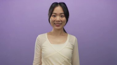 Gülümseyen bir kadın, mor bir arkaplan karşısında arkadaşça bir ifadeyle elini uzatarak izole edilmiş bir stüdyoda evrensel bir hoş geldin jesti sergiliyor..