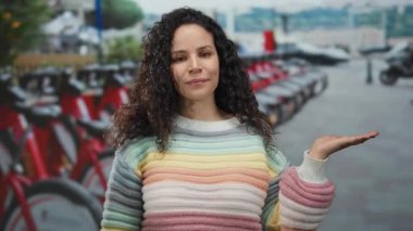 Kıvırcık saçlı genç İspanyol kadın, şehir sokağının önünde sıra sıra bisikletlerle el ele tutuşarak açık havada dostane ve misafirperver bir ortam yaratıyor..