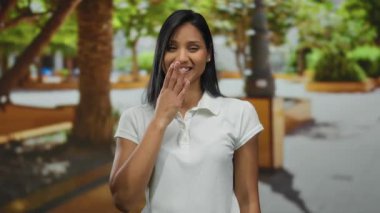 Parktaki genç İspanyol kadın kameraya öpücük yolluyor. Çevresi yeşillik ve şehir manzarasıyla çevrili. Dışarıdaki sıcaklığı ve arkadaşlığı ifade ediyor..