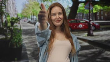 Beyaz bir kadın, güneşli bir sokakta ağaçlarla ve park halindeki bir arabayla el ele tutuşuyor. Onaylandı..