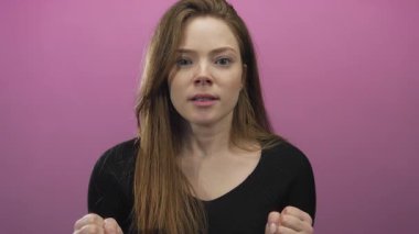 Kadın yumruklarını sıkıyor ve elini kaldırıyor. Stüdyoda pembe arka planda geniş bir sırıtış ve neşeli bir ifadeyle..