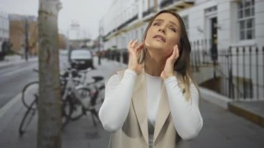 Şehir sokaklarında gürültü nedeniyle kulaklarını tıkayan kadın, şehir ortamında sıkıntılı bir görünüm sergiliyor, sese karşı duygu ve tepki gösteriyor.
