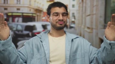 Gözlüklü genç İspanyol adam, güneşli şehir caddesinde avuçlarını dışa doğru kaldırıyor..