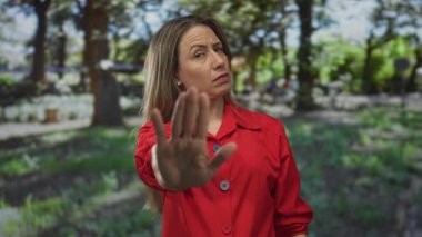 Avuç içleri açık kırmızı ceketli sarışın kadın yeşil ormanda dur hareketi, reddedilme meydan okuması..