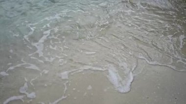 Mallorca 'da kumlu bir sahilde dalgalanan hafif dalgalar berrak mavi su ve yumuşak köpükle sakin bir plaj sahnesi yaratır..