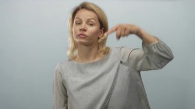 Genç sarışın kadın mavi bir stüdyoda işaret parmağıyla işaret ediyor ciddi bir bakışla, kendine güvenle..