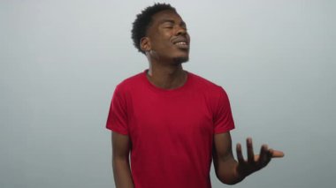 Adam başını eğer ve soluk mavi arka plan ile stüdyoda yukarı bakar kırmızı tişört giyerek; belirsizlik iç gözlem.