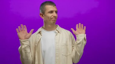 Canlı mor bir duvara karşı elleri havada bir adam omuz silkme ile umursamazlık gösteriyor. Belirsizlik ve tuhaf bir tepki gösteriyor.