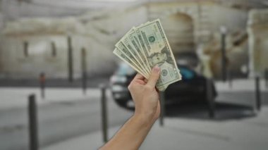 Bir şehir caddesinde Amerikan Doları banknotları tutan adam açık havada şehir geçmişi bulanık, açık hava ortamında finans, para ve ekonomiyi ön plana çıkarıyor..