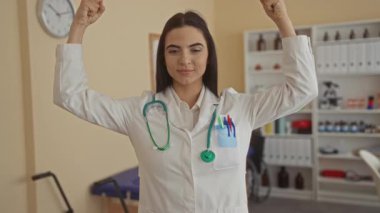 Steteskoplu İspanyol kadın doktor klinikte güçlü kol hareketleri yapıyor. Sağlık hizmetleri işyerinde güven ve yetkilerini dile getiriyor..