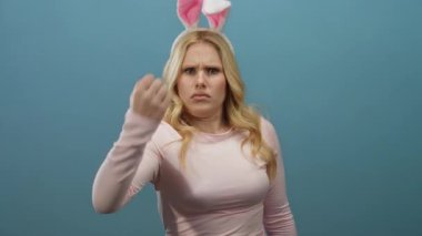 Tavşan kulağı takan bir kadın, mavi arka plana karşı komik, öfkeli bir jest yapıyor, mizahla ifadeyi neşeli bir ortamda birleştiriyor..