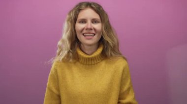 Kadın kamerayla konuşurken elini hareket ettiriyor. Sarışın, genç, gülümseyen bir stüdyo resmi..