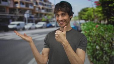 Bulanık trafik arkaplanı ve kaldırım çizgilerine karşı güneşli şehir caddesinde boş kaldırıma doğru avuç içi açık jestler yapan genç adam;.