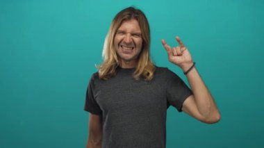 Sarışın, uzun saçlı, çıplak kollu sırıtan ve stüdyoda rock boynuzlarını gösteren bir adam..