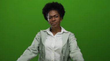 Gözlüklü bir kadın, neşeli, eğlenceli ve kaygısız bir tavır sergileyerek, canlı yeşil bir arka plan karşısında, kulaklarını şakayla kapatır ve dilini dışarı çıkarır..