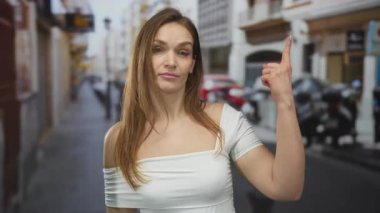 Bulanık scooterlar ve arabalarla dolu bir şehir caddesinde sağ eliyle baş parmak hareketi yapan bir kadın..