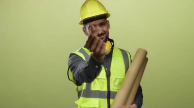 Güvenlik yeleği giyen İspanyol bir adam kalp hareketi yapıyor. Sarı arka planda parmaklarıyla. İnşaat bağlamında sıcaklığı ve dostluğu simgeliyor..