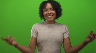 Genç Afrikalı Amerikalı kadın gülümsüyor ve yeşil stüdyo arkaplanına parmak ucuyla işaret ediyor..
